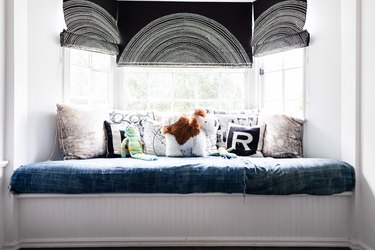 A window seat with decorative roller shades hung in the window