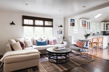 A living room with neutral shades on the window and a tan sectional