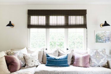 white sofa with purple and blue pillows in a room with woven shades and industrial wall sconces