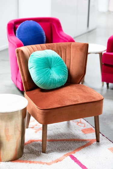 Brown velvet accent chair, round turquoise pillow, gold drum side table, Fuchsia chair, blue pillow, orange diamond rug.