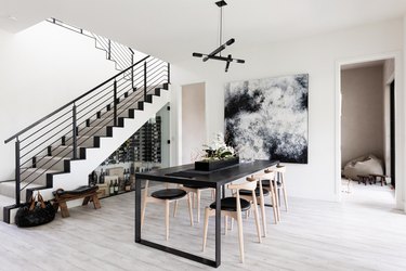 Dining room with gray wood floors, black furniture, contemporary art and staircase