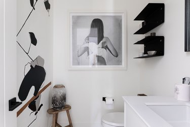 White walled bathroom with black shelving, wall decals and photograph art