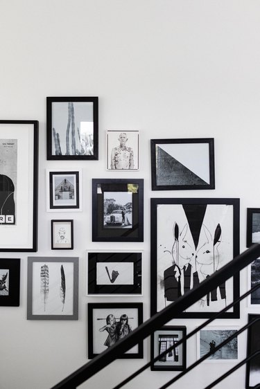 Staircase idea with art framed in black frames on a wall next to a black banister
