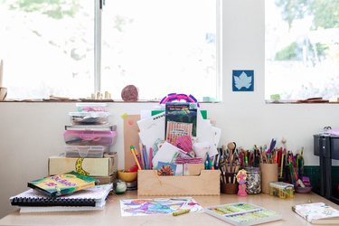A kid's art table with various supplies facing windows
