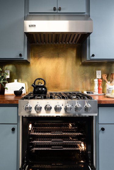 Brass backsplash behind stove in kitchen with blue painted cabinets.