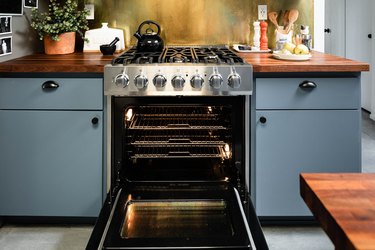 Gas stove with oven door open; brass backsplash and blue cabinets