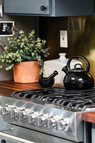 Gas stove with black kettle, white bread box and plant on countetrop