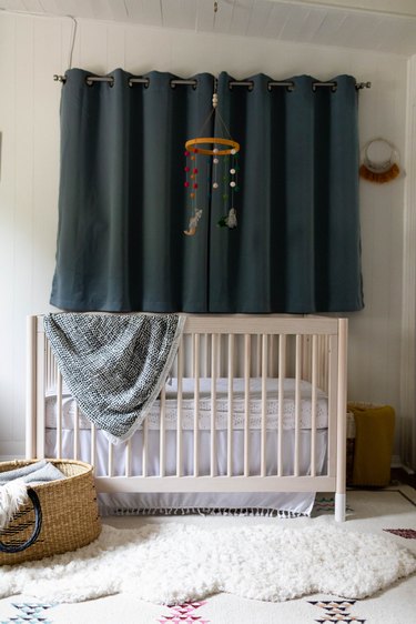 A minimalist nursery with a white crib and a blue curtain