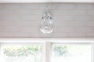 A globe wall light hanging on a cinder block wall above a window.