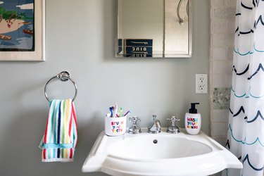 A pedestal sink with an overflow hole and colorful towel and shower curtain