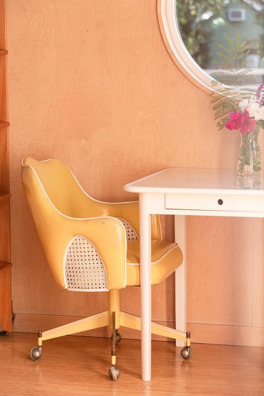 yellow leather desk chair and white small desk with flower vase on top