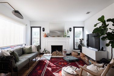 A white living room with a red rug, white fireplace, and a roller shade on the window