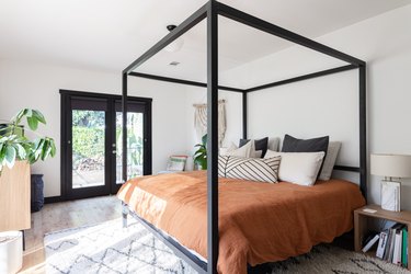 A four-post bed with light brown bedding in a bedroom with French doors leading out to the backyard