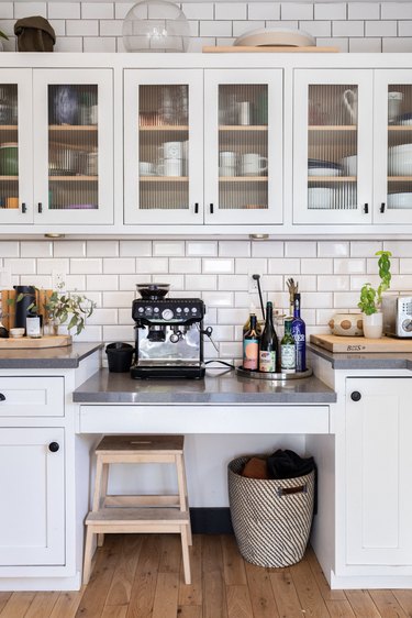 White kitchen cabinets with glass doors, a subway tile backsplash and an espresso machine amongst other kitchen accessories