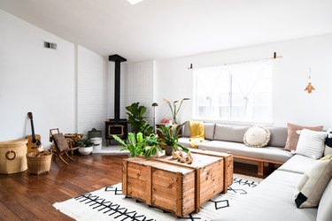 Living room with long gray sofa, wood crate coffee table, plants, and antique stove
