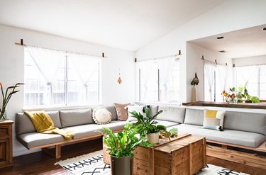 Long gray sofa, wood crate coffee table in living room with curtained windows