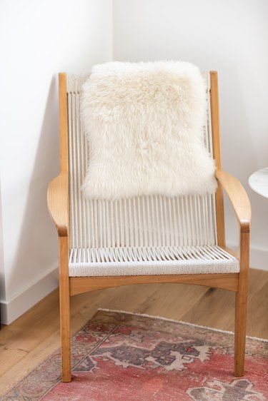 Accent chair with wood armrests and white fur blanket on hardwood floor with red rug