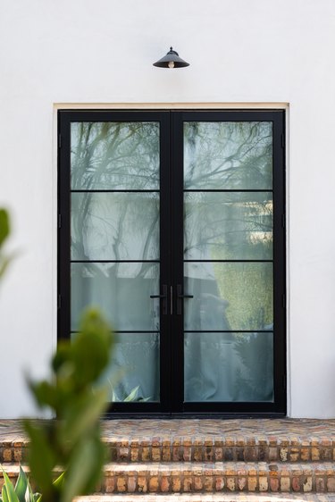 Black framed French doors and brick steps of a white house