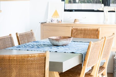 Dining table with table runner and bowl with wicker chairs