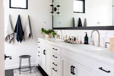 White bathroom vanity with black drawer handles under a large mirror
