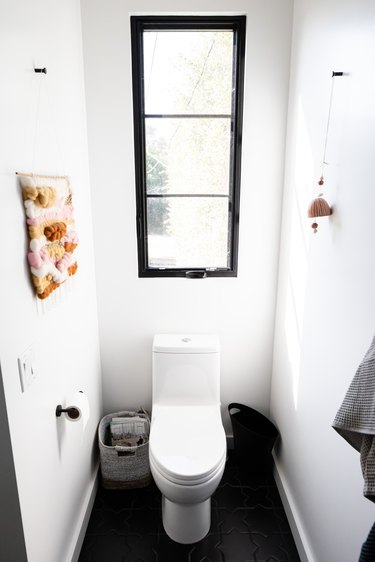 White-walled bathroom with a long black framed window over a toilet