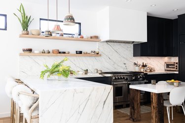 White walled kitchen with dark gray cabinets, plants and wood floors