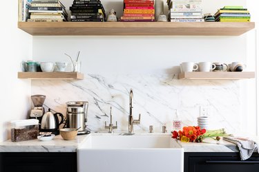 White calcutta wall of a kitchen with white sink and wood shelving with books