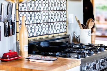 A wood kitchen counter with a stovetop and colorful tile backsplash