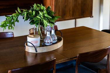 A wood dining table and a wood tray with a plant and condiment bottles