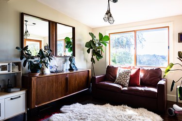 A boho styled living room with cushions, wood sideboard and plants