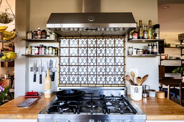 Kitchen with stainless steel oven and oven hood with tile backsplash and gray walls, and shelving on both sides and wood countertop
