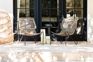 Three wicker patio chairs on a front porch by black framed windows