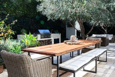 A wood table with metal benches and wicker chairs on a paver patio