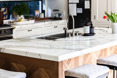 A wood kitchen island with white granite countertops in a white cabinet kitchen