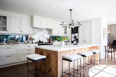 A kitchen with stove vent, white cabinets, contemporary light fixture and wood kitchen island