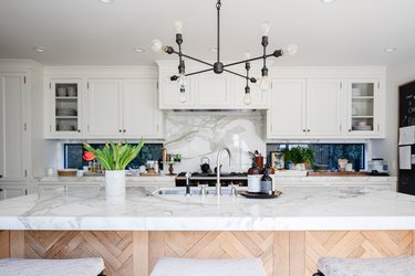 A kitchen with white cabinets, contemporary light fixture and wood kitchen island