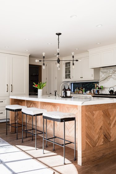 A wood kitchen island with a contemporary light fixture and white walls