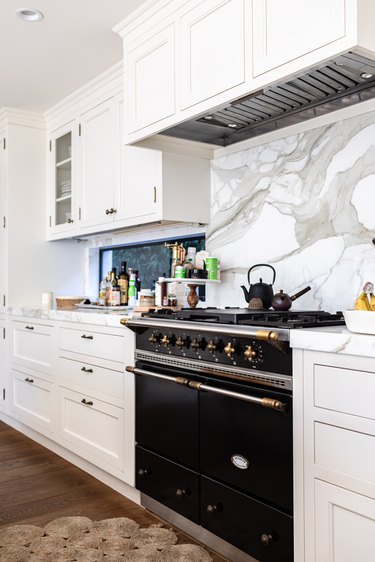 A kitchen with white cabinets, marble backsplash and wood floors