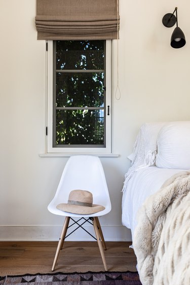 A white chair with a hat and a window with a brown window shade
