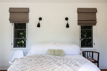 Bedroom with white bedding, brown window shades and black wall lamps