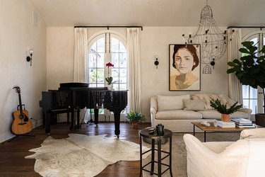 A white walled living room with white furniture, grand piano and chandelier