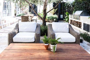 Patio wicker chairs with white cushions with a wood table and plants
