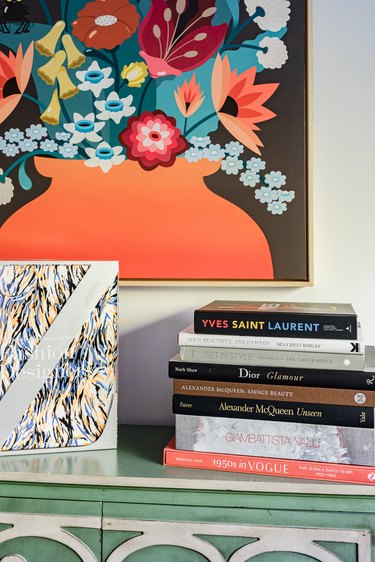 Fashion books on a green and white wood sideboard, and a colorful floral painting.