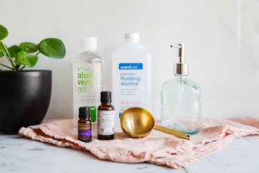 rubbing alcohol, aloe vera gel, essential oil, a measuring cup, and a glass jar with a pump full of diy hand sanitizer
