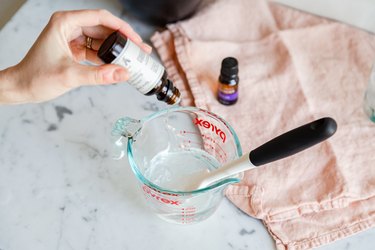 adding drops of essential oil to alcohol and aloe vera in a measuring cup