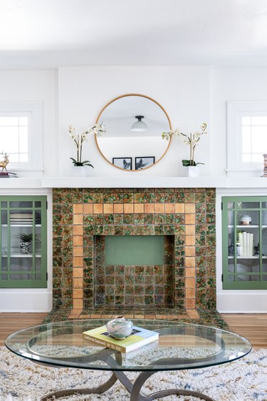 living room with green and gold tiled fireplace and sage green cabinets
