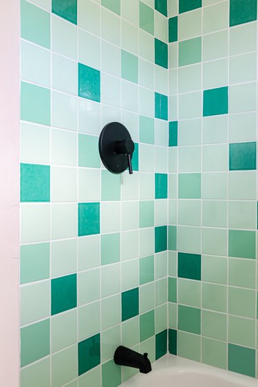 Multiple shades of green ceramic tile in bathroom, black faucet.