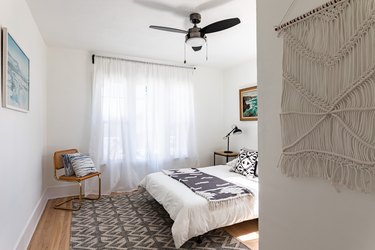 A bedroom with a macrame hanging and sheer curtains hung