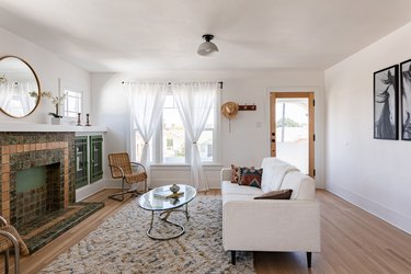 A living room with sheer curtains, light wood flooring and a white couch