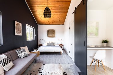 Bold boho bedroom with wood floor and ceiling, gray-black accents, and a white minimalist office